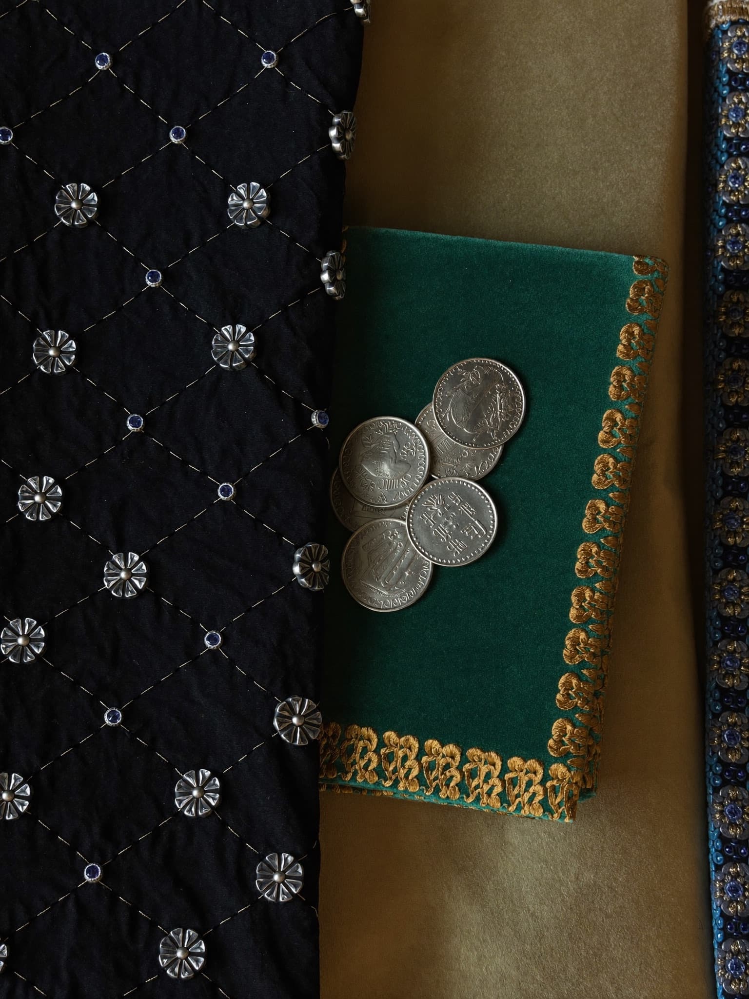 Dark macro textile waves with red silk, black velvet, gold embroidery, silver coins, and lapis beads.
