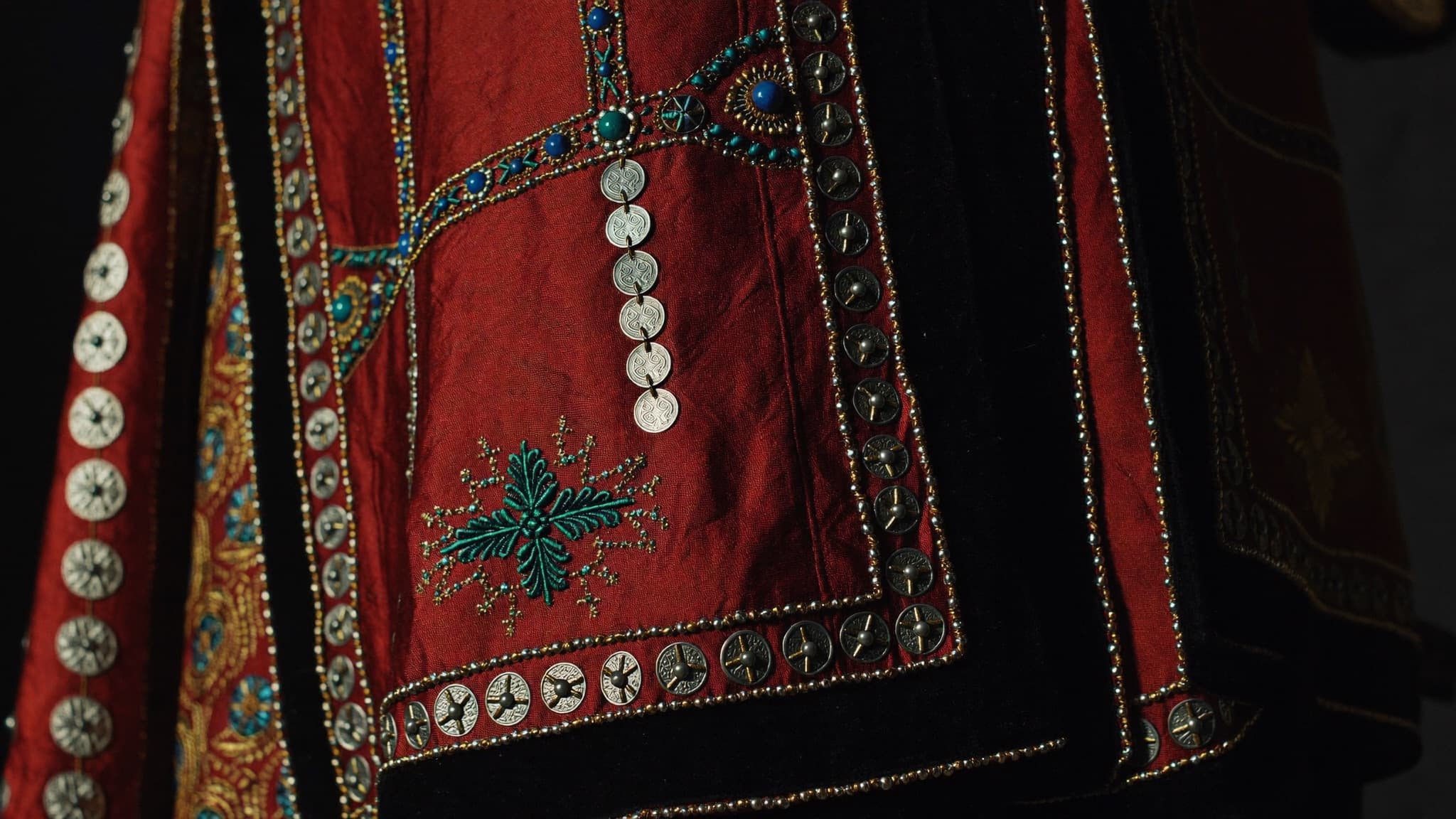 Rows of coins and beadwork stitched across red silk — sina-band detail.